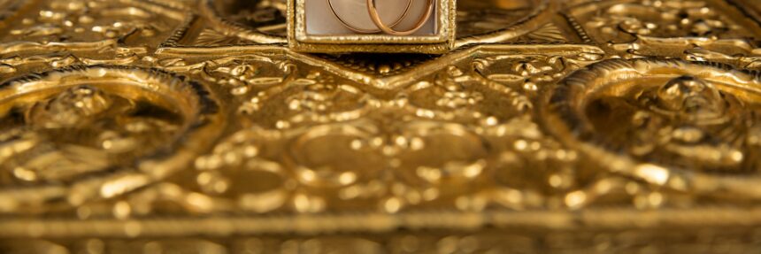 Close-up of gold wedding rings and a delicate tiara on an ornate golden background, symbolizing luxury and elegance.