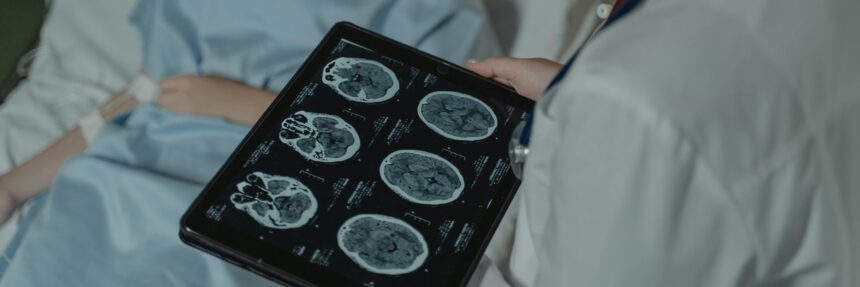 A doctor analyzes brain scans on a digital tablet beside a patient in a hospital bed.